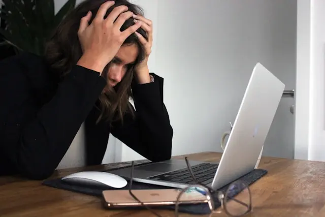 mujer tomandose la cabeza frente a la laptop