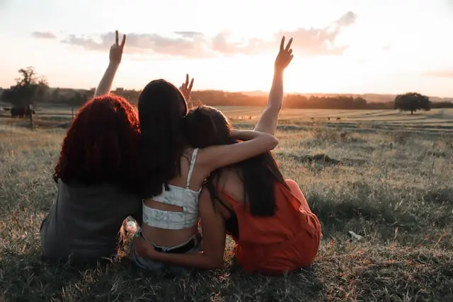 tres mujeres sentadas de espalda y alzando las manos