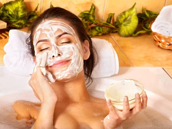 Mujer sonriente en spa aplicandose una de las mejores mascarillas faciales caseras.