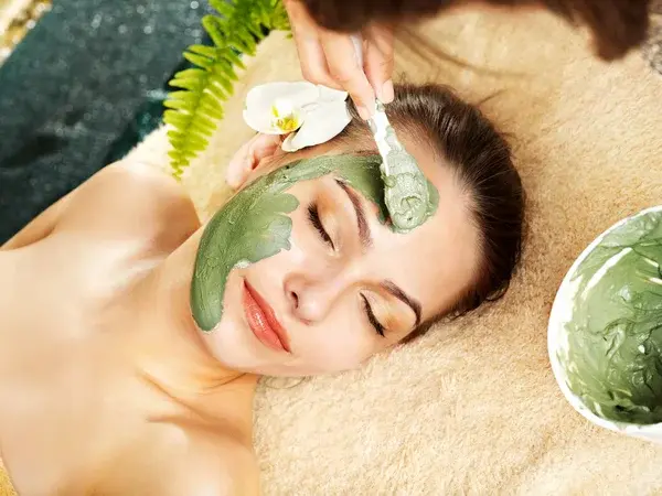 Mujer echada con un tipo de mascarilla verde.